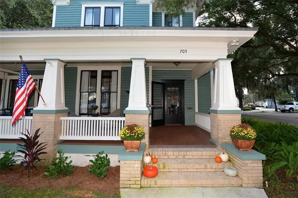 a view of a white house with a yard plants and large tree