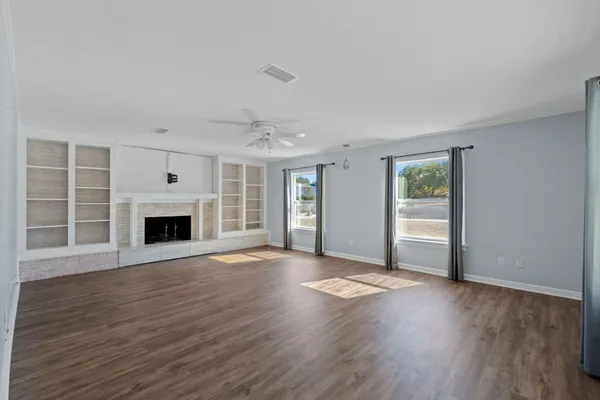 an empty room with wooden floor fireplace and windows