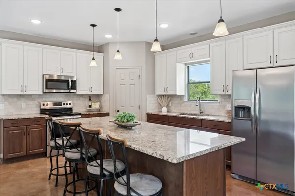 a kitchen with stainless steel appliances granite countertop a sink a stove a refrigerator cabinets and chairs