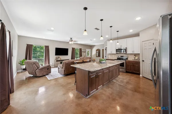 a large kitchen with stainless steel appliances kitchen island granite countertop a lot of cabinets a refrigerator and a stove