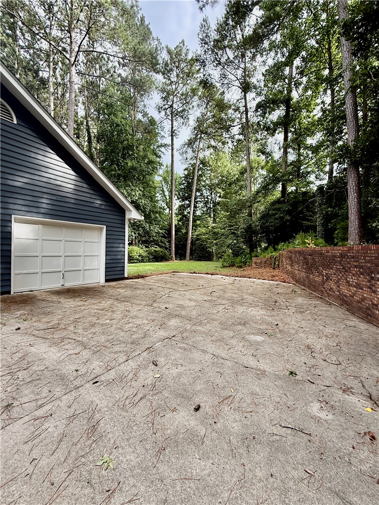 235 Stonehaven Way Seneca, SC 29672 - Photo 9 of 35 A well-maintained concrete driveway leads to a classic white garage door, nestled amongst mature trees and a brick retaining wall.