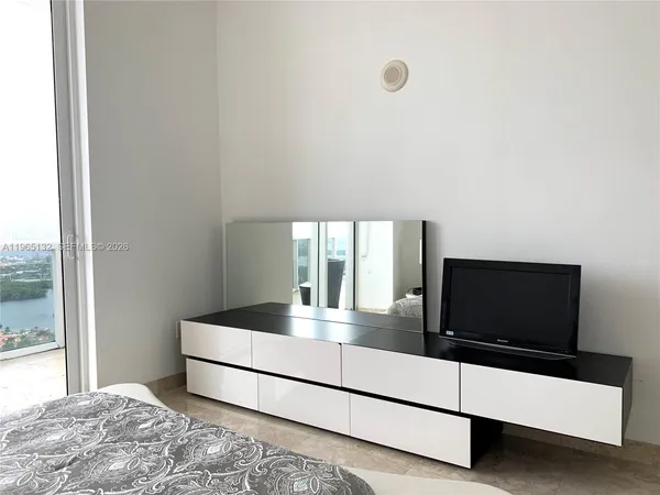 a living room with a bed and a flat tv screen on the dresser
