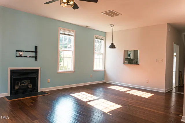 a view of an empty room with wooden floor fireplace and a window