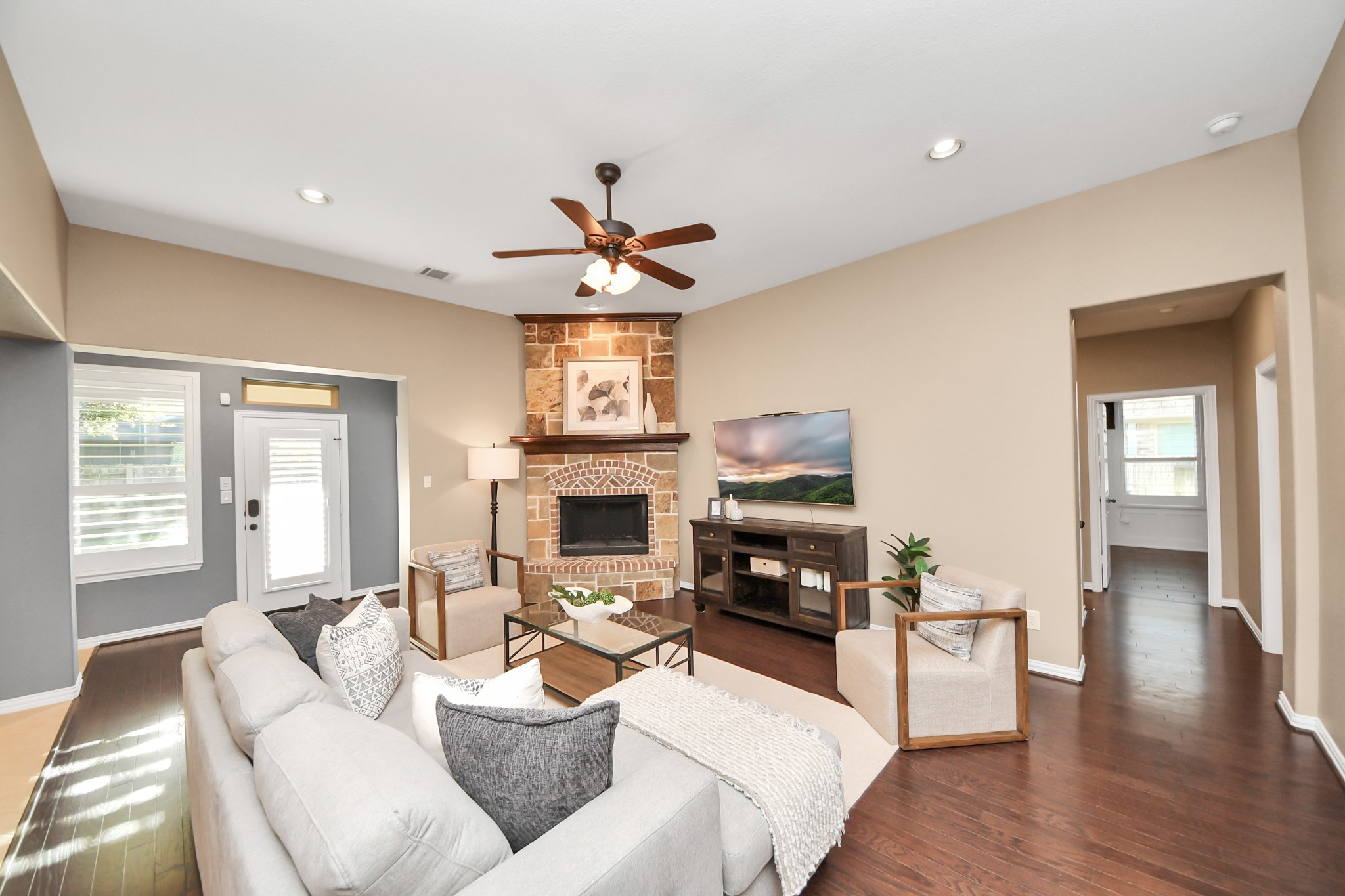 3115 Currant Drive Manvel, TX 77578 - Photo 9 of 48 This inviting living room features a cozy stone fireplace, modern ceiling fan, and ample natural light. The space is complemented by hardwood floors, neutral walls, and a comfortable seating arrangement, creating a warm and stylish atmosphere.