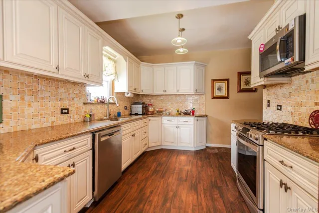 a kitchen with stainless steel appliances granite countertop a stove a sink dishwasher and white cabinets with wooden floor