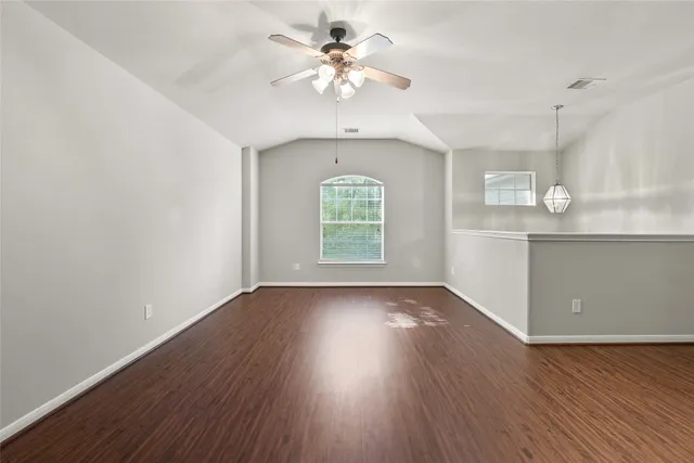an empty room with wooden floor chandelier fan and windows