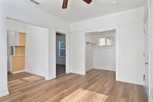an empty room with wooden floor ceiling fan and windows