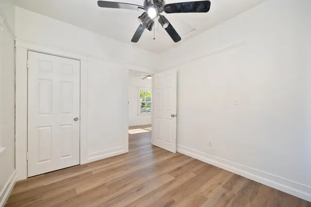 an empty room with wooden floor fan and windows