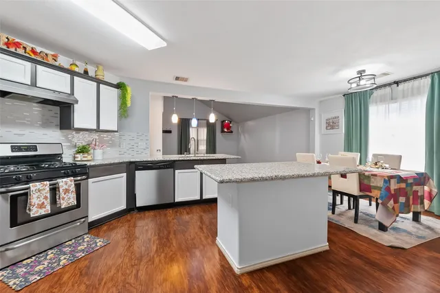 a large kitchen with stainless steel appliances a stove a sink dishwasher and a dining table with wooden floor