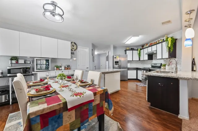 a open kitchen with stainless steel appliances granite countertop a stove top oven a refrigerator a sink dishwasher and white cabinets with wooden floor