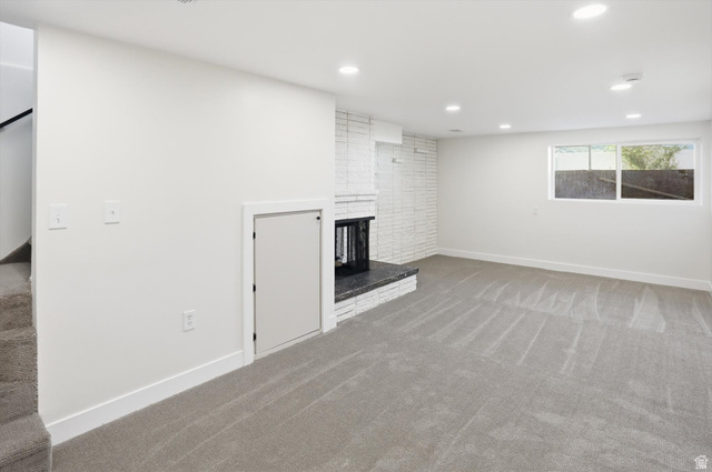 810 East Maple Street Mapleton, UT 84664 - Photo 22 of 49 Spacious living area featuring light gray carpeting, recessed ceiling lighting, a brick fireplace with a dark stone hearth, a multi-pane window, and white painted walls