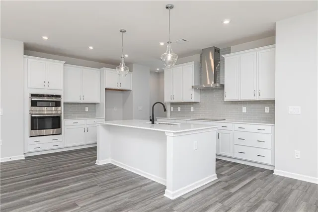 a large kitchen with granite countertop a stove a sink and white cabinets with wooden floor