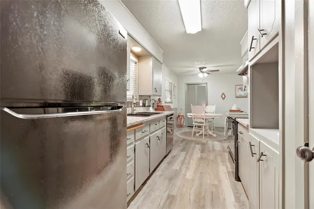 a kitchen with stainless steel appliances granite countertop a refrigerator a sink dishwasher a stove and white countertops with wooden floor