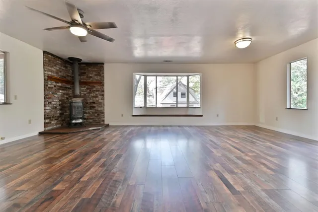 an empty room with wooden floor chandelier fan and windows
