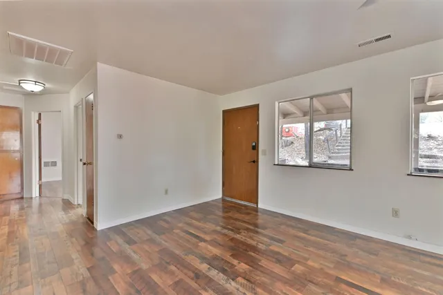 a view of an empty room with wooden floor and a window