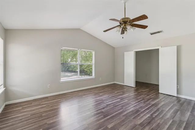 an empty room with wooden floor fan and windows