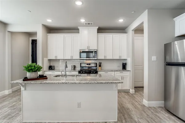 a kitchen with stainless steel appliances kitchen island granite countertop a refrigerator a stove a sink and white cabinets with wooden floor