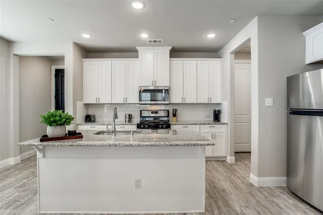 a kitchen with stainless steel appliances kitchen island granite countertop a refrigerator a stove a sink and white cabinets with wooden floor