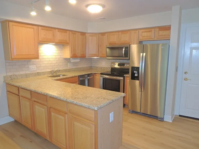 a kitchen with stainless steel appliances granite countertop a refrigerator a sink dishwasher a stove and white countertops with wooden floor