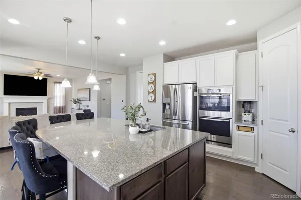 a kitchen with stainless steel appliances granite countertop a kitchen island a stove a refrigerator a oven a sink a dining table and chairs with wooden floor