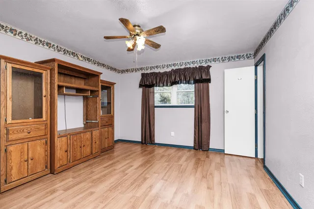 an empty room with wooden floor chandelier fan and windows