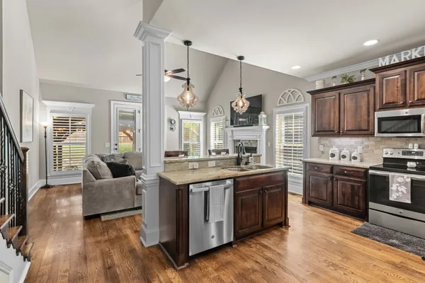 a kitchen with stainless steel appliances granite countertop a stove top oven a sink dishwasher a dining table and chairs with wooden floor