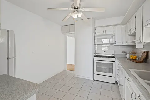 a kitchen with granite countertop a stove a sink and a refrigerator with white cabinets