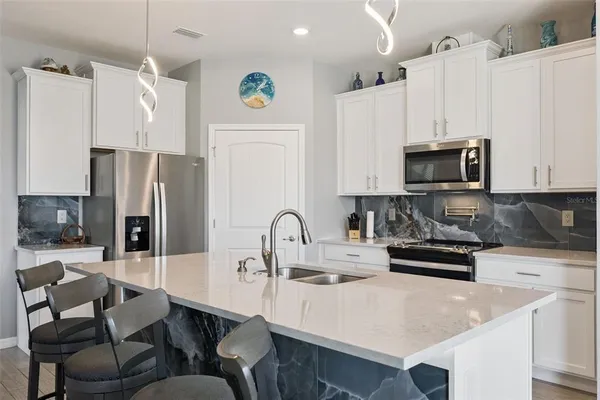 a kitchen with stainless steel appliances a refrigerator a sink a stove a dining table and chairs with wooden floor