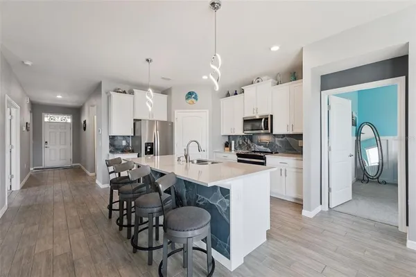 a kitchen with stainless steel appliances kitchen island granite countertop a refrigerator a stove a sink a dining table and chairs with wooden floor