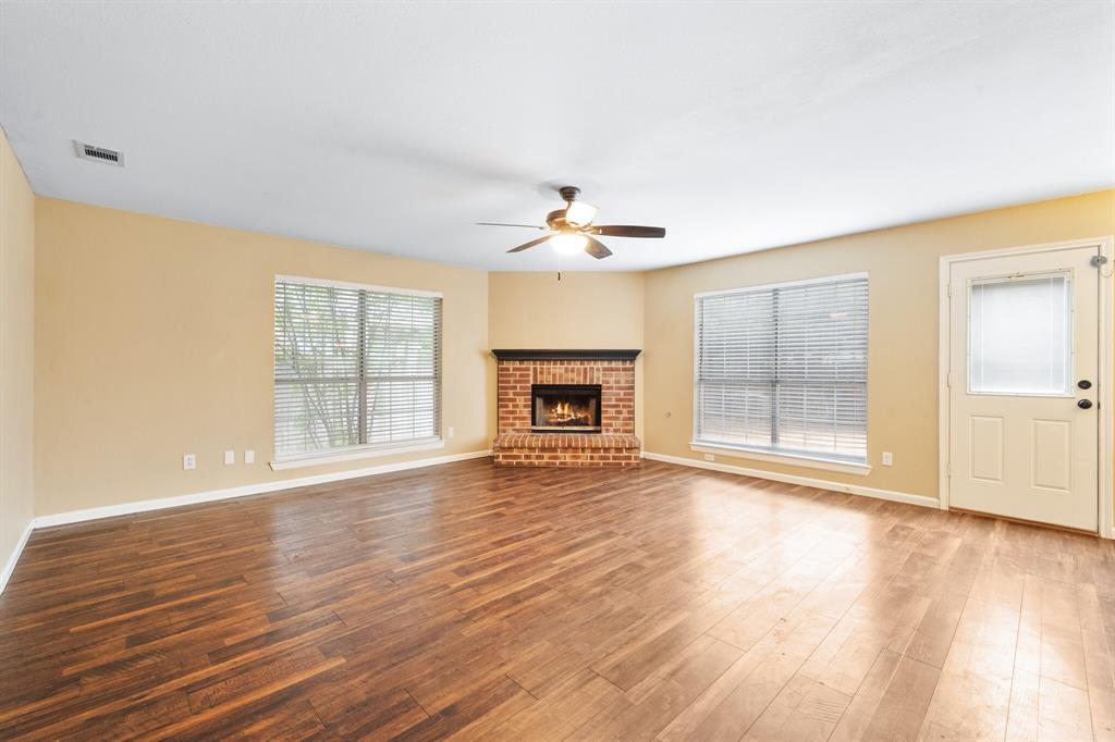 7517 Point Reyes Drive Fort Worth, TX 76137 - Photo 8 of 30 Spacious interior featuring wood-finish flooring, a brick fireplace with a dark mantel, and multiple windows with blinds