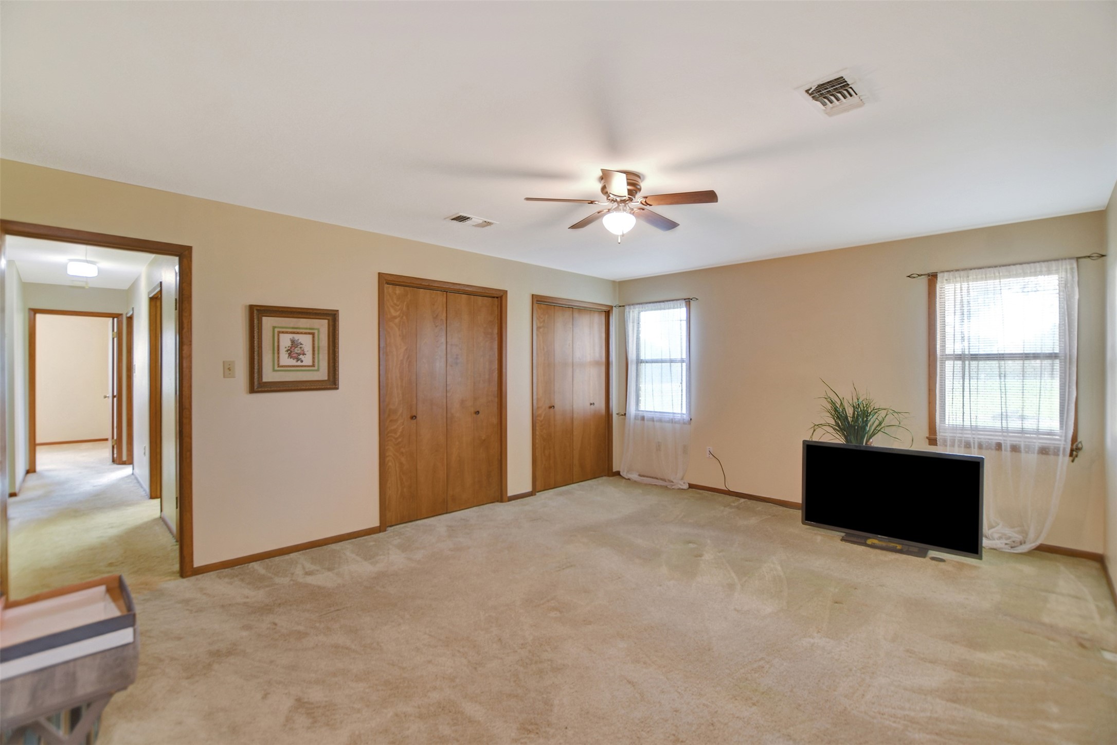 341 South S Loop Bellville, TX 77418 - Photo 20 of 33 This spacious bedroom features neutral carpeting, a ceiling fan, and ample natural light from two windows. It includes two wooden closets for storage and has a hallway leading to other rooms.