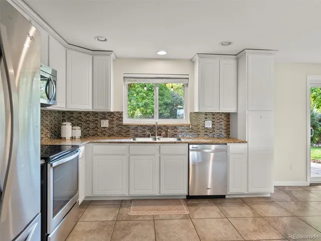a kitchen with granite countertop white cabinets white appliances a sink and a window