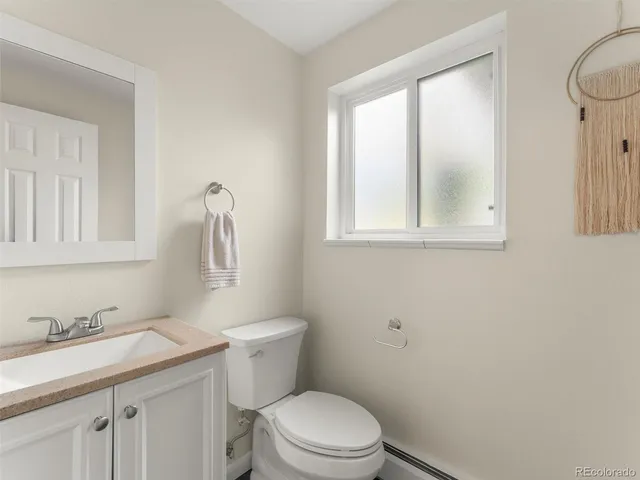 a bathroom with a granite countertop toilet a sink a mirror and a window