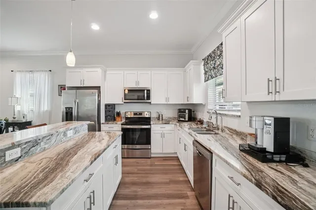 a kitchen with stainless steel appliances granite countertop a stove top oven a sink dishwasher and a refrigerator with wooden floor