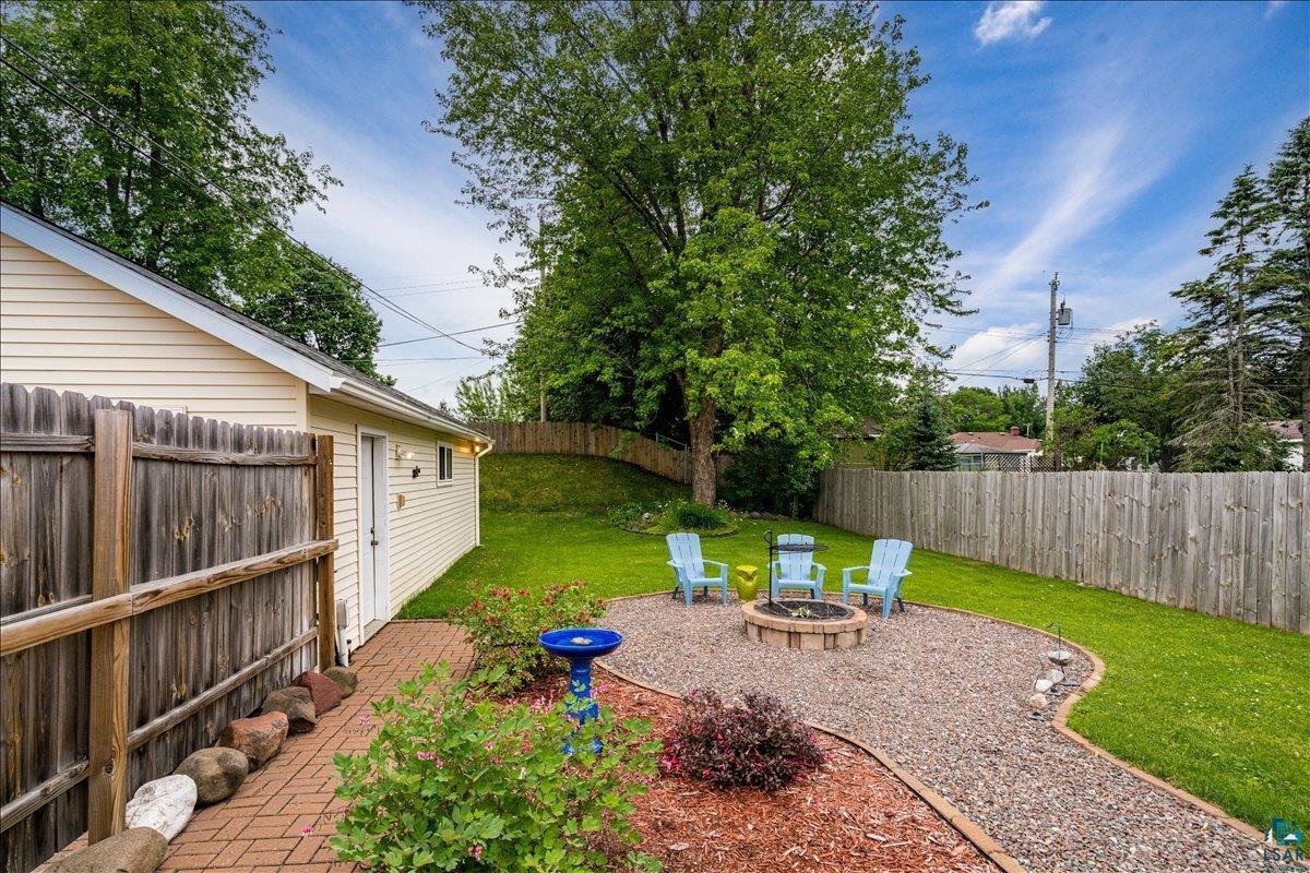 130 West Austin Street Duluth, MN 55803 - Photo 23 of 35 Private backyard featuring a paver brick pathway, a gravel fire pit area, mature landscaping, and a wood privacy fence