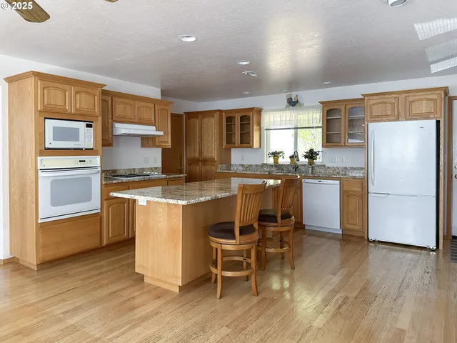 a kitchen with stainless steel appliances granite countertop a refrigerator a stove top oven a sink dishwasher and white cabinets with wooden floor