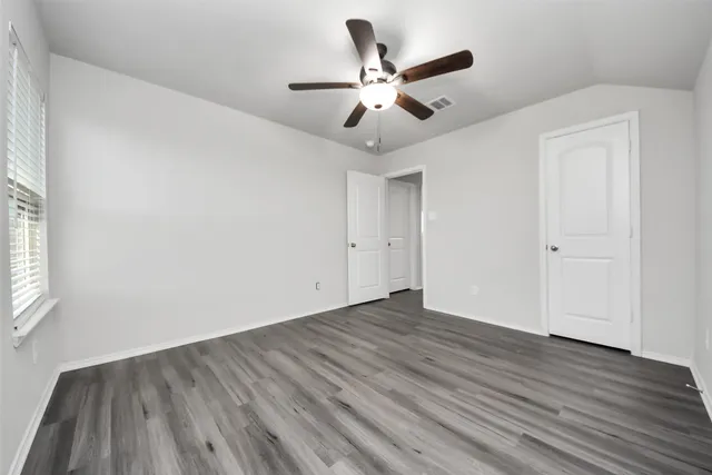 an empty room with wooden floor fan and windows