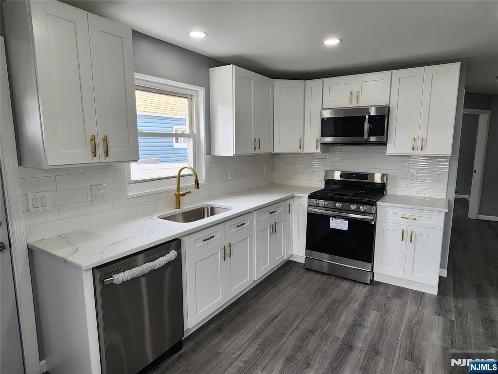 111 Church Street Lodi, NJ 07644 - Photo 7 of 21 a kitchen with stainless steel appliances white cabinets a sink a stove a microwave and wooden floors