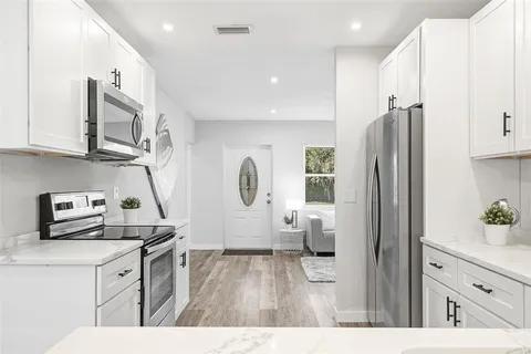 a kitchen with stainless steel appliances a refrigerator a sink a stove and white cabinets with wooden floor