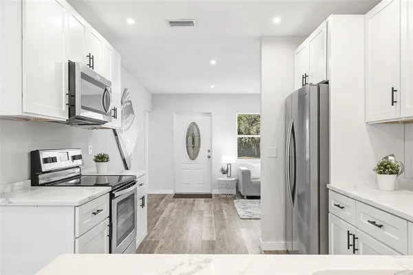 a kitchen with stainless steel appliances a refrigerator a sink a stove and white cabinets with wooden floor