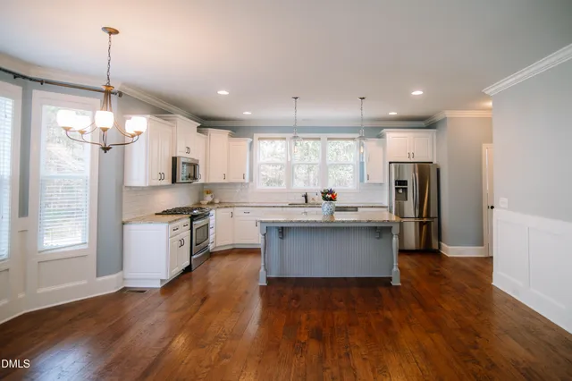 a kitchen with stainless steel appliances kitchen island a refrigerator a sink dishwasher a stove and white cabinets with wooden floor