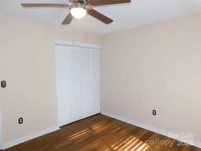 a view of an empty room with wooden floor and a ceiling fan