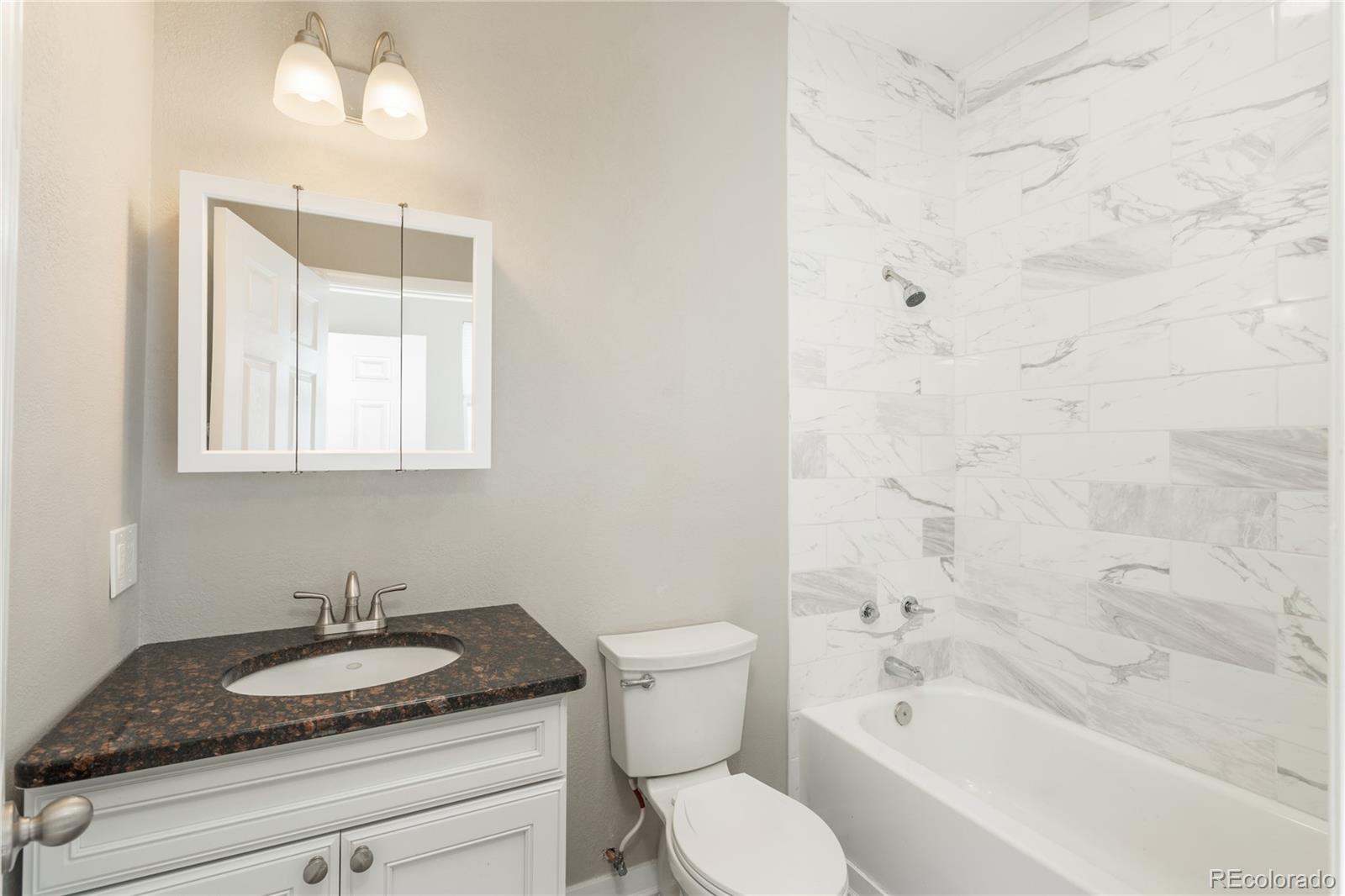 4695 Parfet Street Wheat Ridge, CO 80033 - Photo 34 of 46 a bathroom with a granite countertop sink a toilet and bathtub