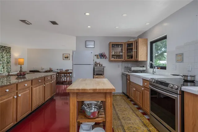 a kitchen with stainless steel appliances granite countertop a stove top oven a sink dishwasher a dining table and chairs with wooden floor