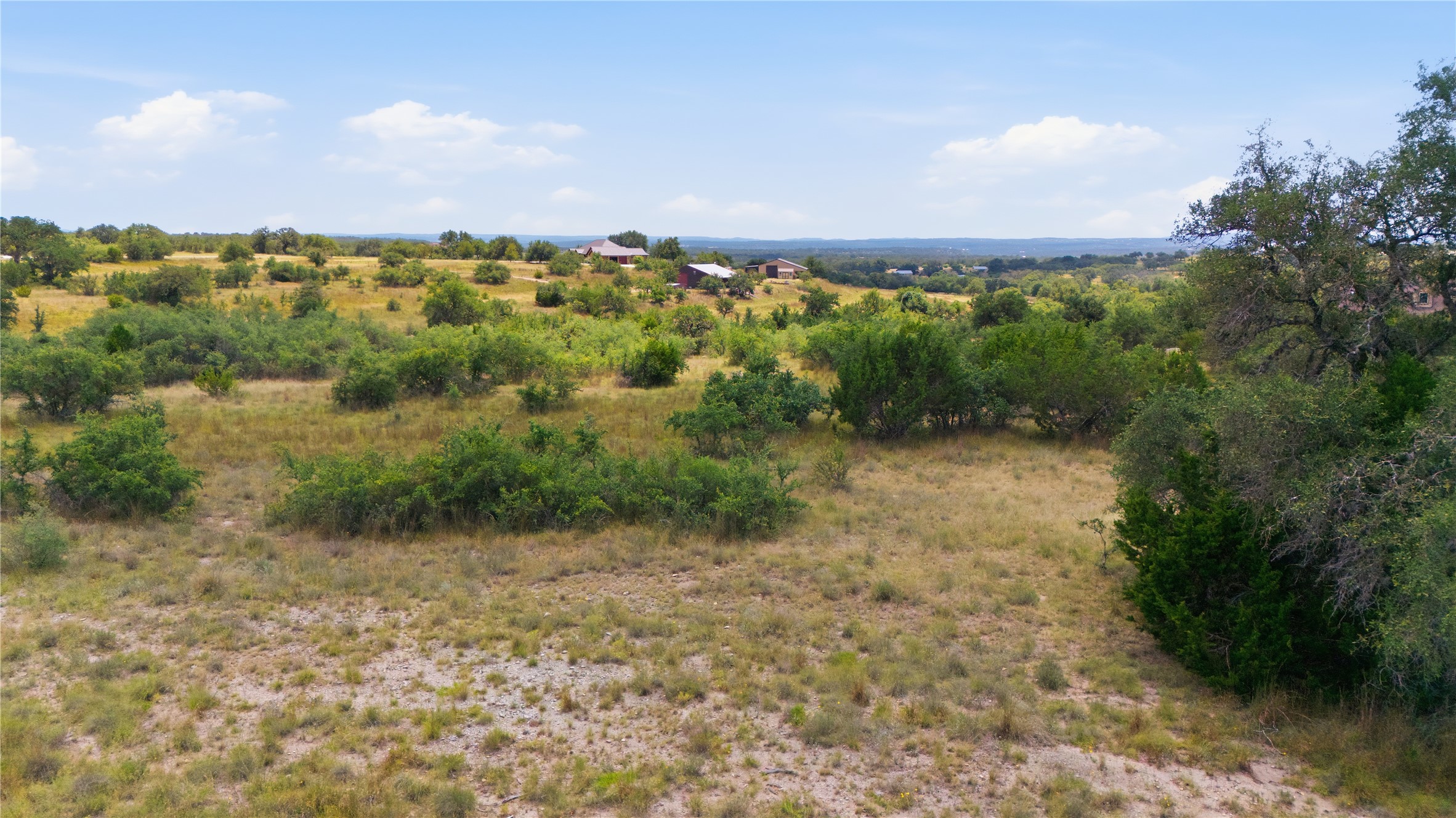 963 Summit Ridge Trail Johnson City, TX 78636 - Photo 28 of 30 Vast, open terrain featuring scattered green foliage and distant structures under a broad, bright sky.