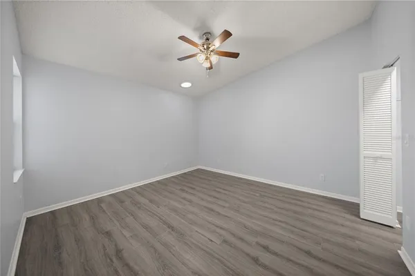 a view of an empty room with wooden floor and a ceiling fan