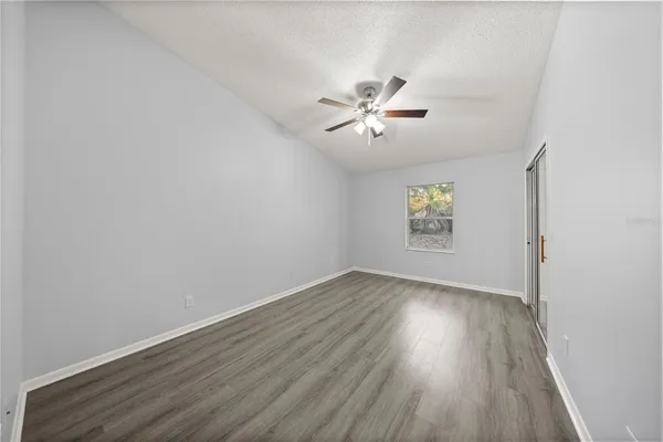an empty room with wooden floor chandelier fan and windows