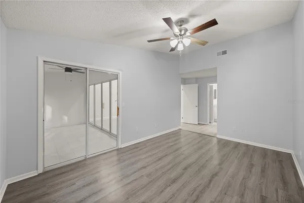 a view of an empty room with wooden floor and a ceiling fan