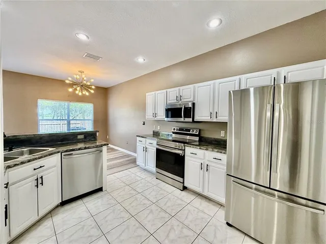 a kitchen with stainless steel appliances granite countertop a refrigerator a stove a sink and white cabinets with wooden floor