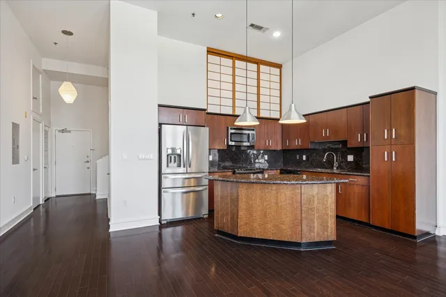 a kitchen with stainless steel appliances granite countertop a refrigerator a sink dishwasher a stove and white countertops with wooden floor